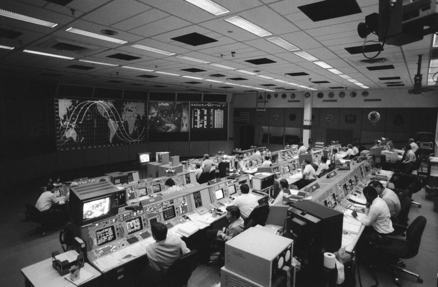Sala de control de misiones de la NASA con muchas personas trabajando en sus estaciones.